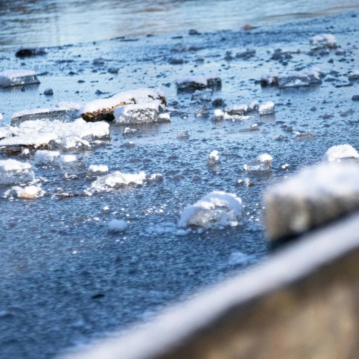 Chunks of broken ice scattered across a frozen, wet pavement, a low wall in the foreground.