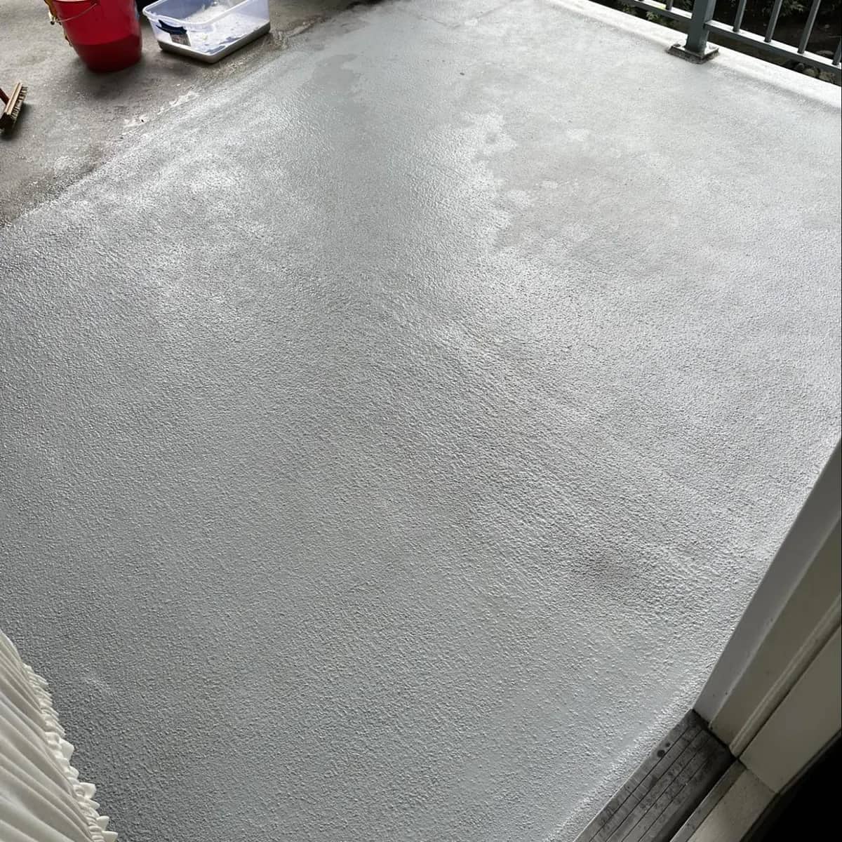 The same condo balcony deck after cleaning, the concrete an even pale grey from the door to the railing.