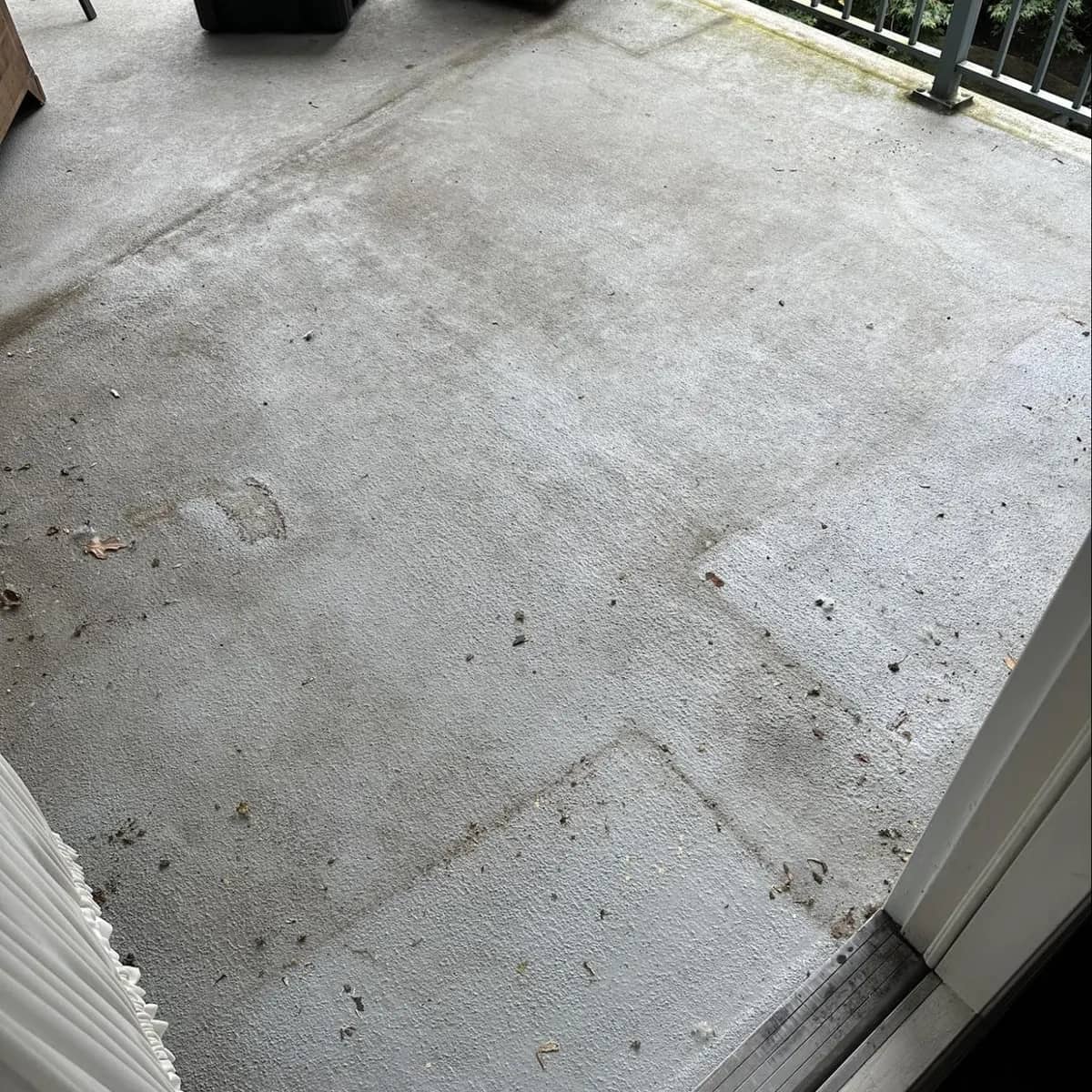 A condo balcony's concrete deck before cleaning, dark with grime, footprints and scattered debris along the railing.