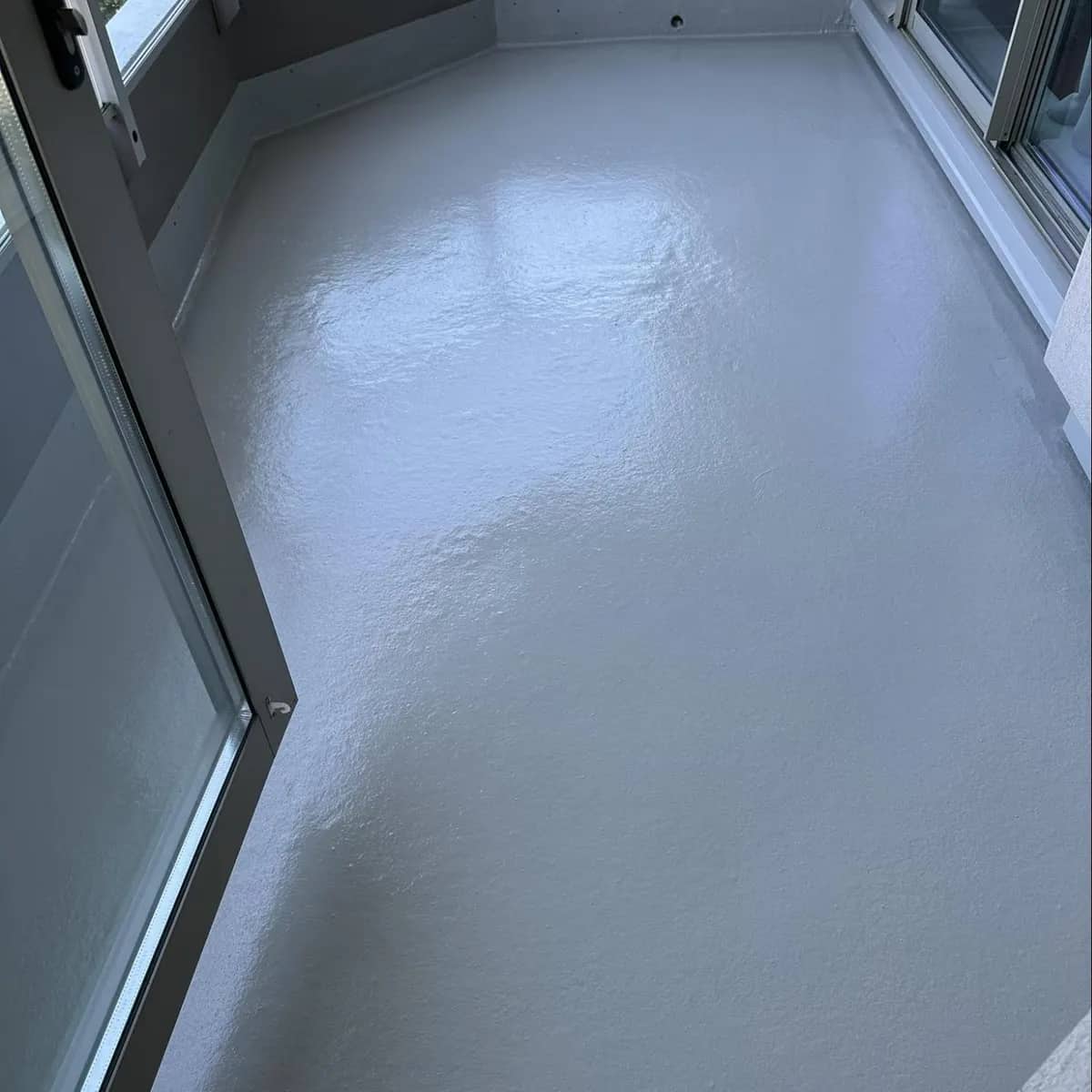 The same enclosed balcony after cleaning, the floor washed to a clean, glossy grey that reflects the windows.