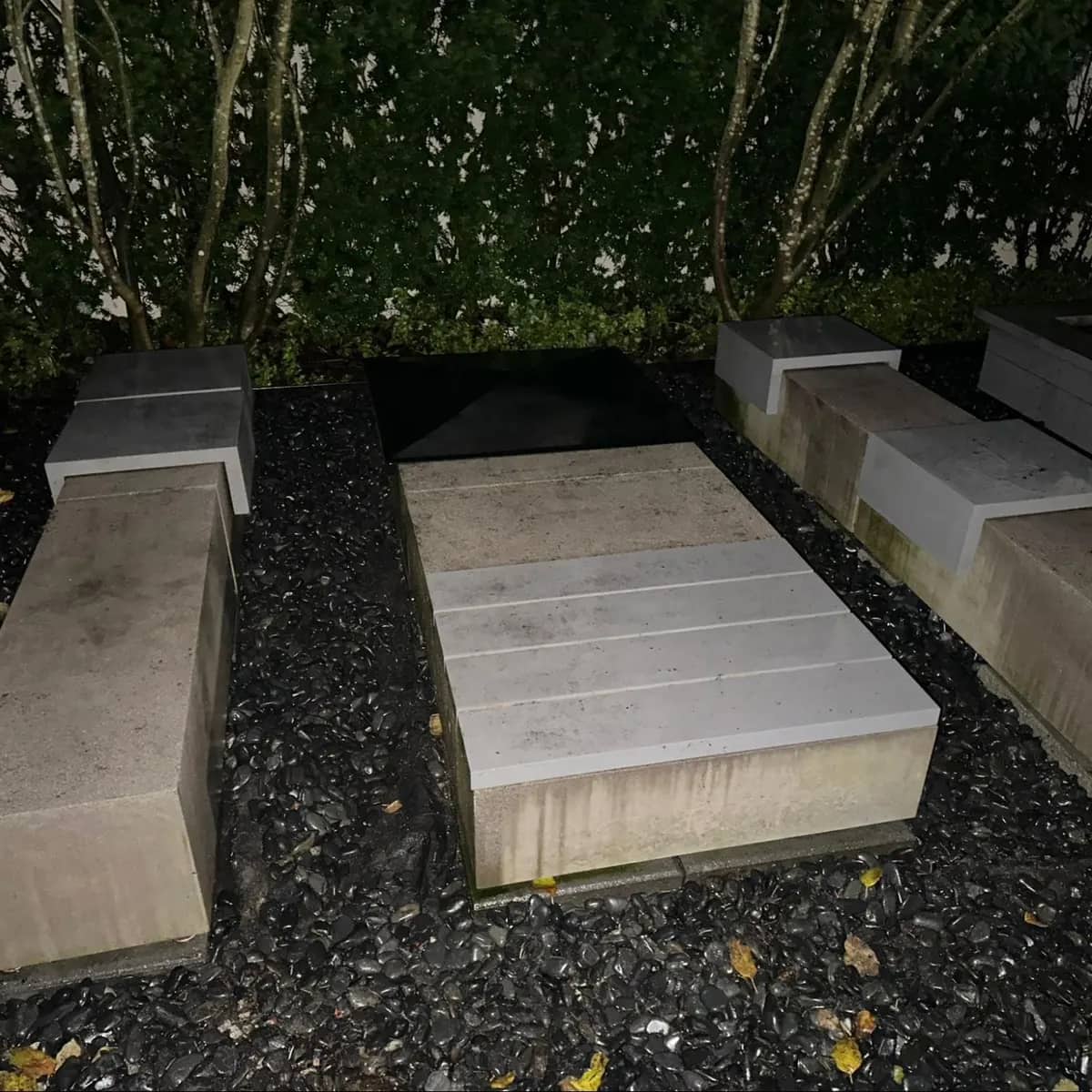 The same concrete garden benches after pressure washing, clean and pale against the dark gravel and hedge.