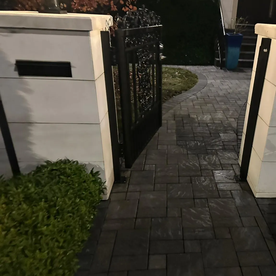 Cream stone gate pillars and the paver walkway between them after pressure washing, clean in the evening light.