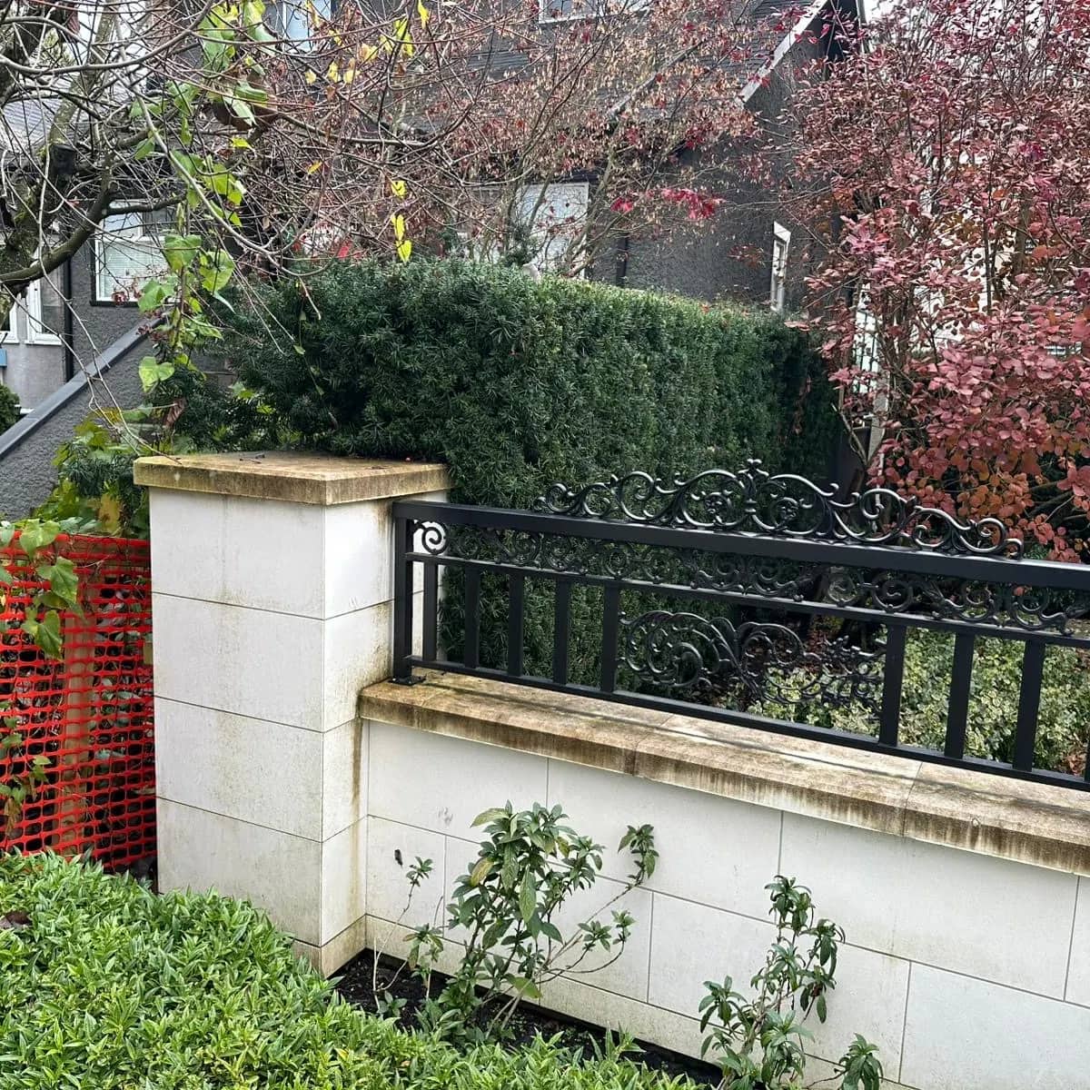 A cream stone garden wall with a wrought-iron railing before washing, its capstones stained dark with dirt and algae.