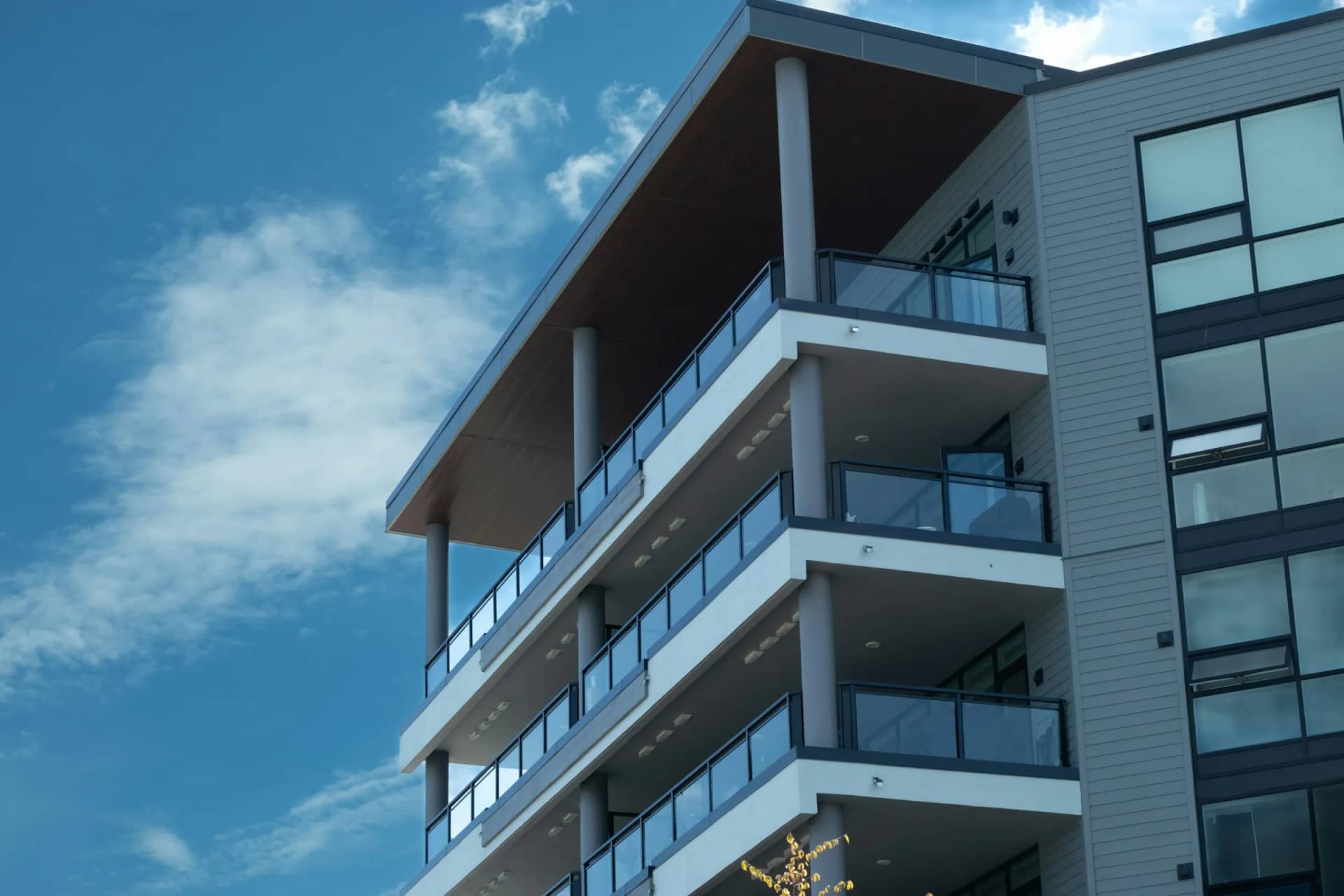 Balcony cleaning: a four-storey condo building with glass-railed balconies stacked one above another under a blue sky.