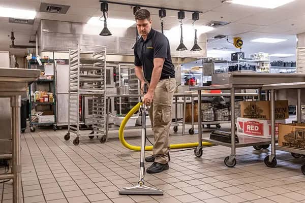 Commercial cleaning: a worker running a floor squeegee across the tiled floor of a commercial kitchen.