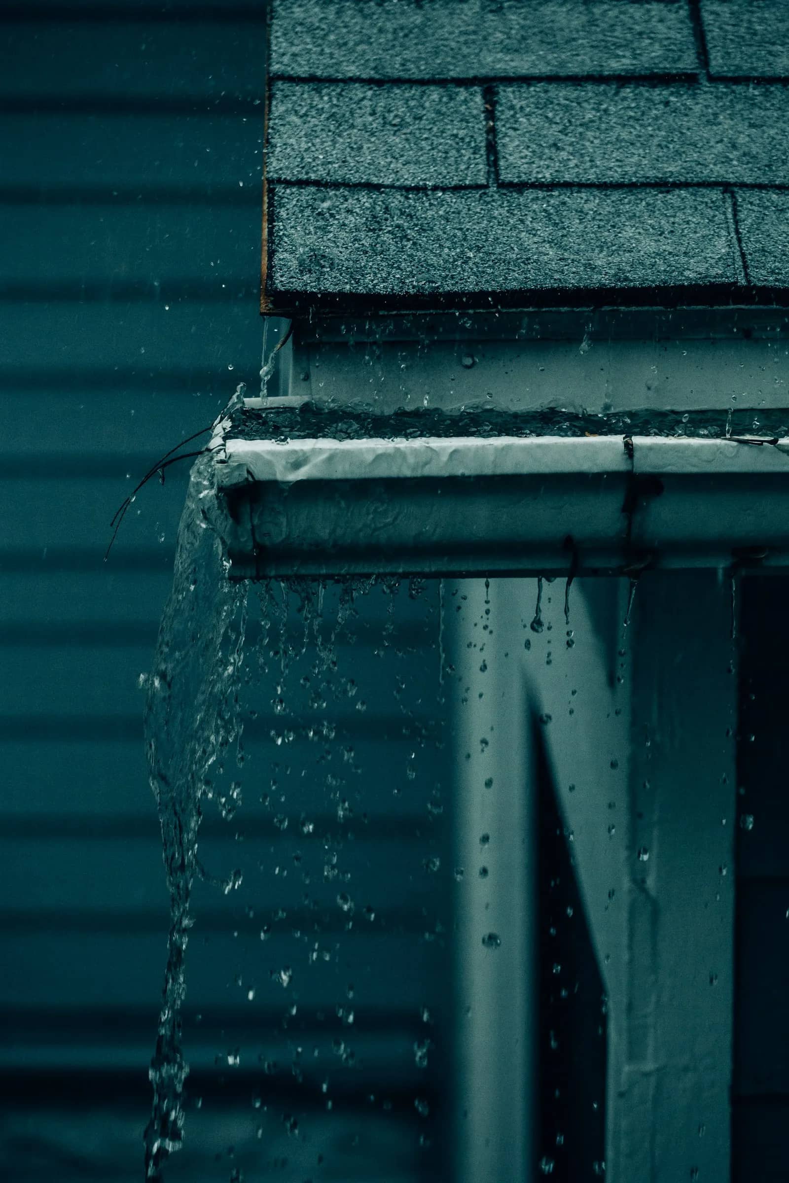 Gutter cleaning: water running the length of a dark green gutter in heavy rain, the channel carrying it along rather than holding it.