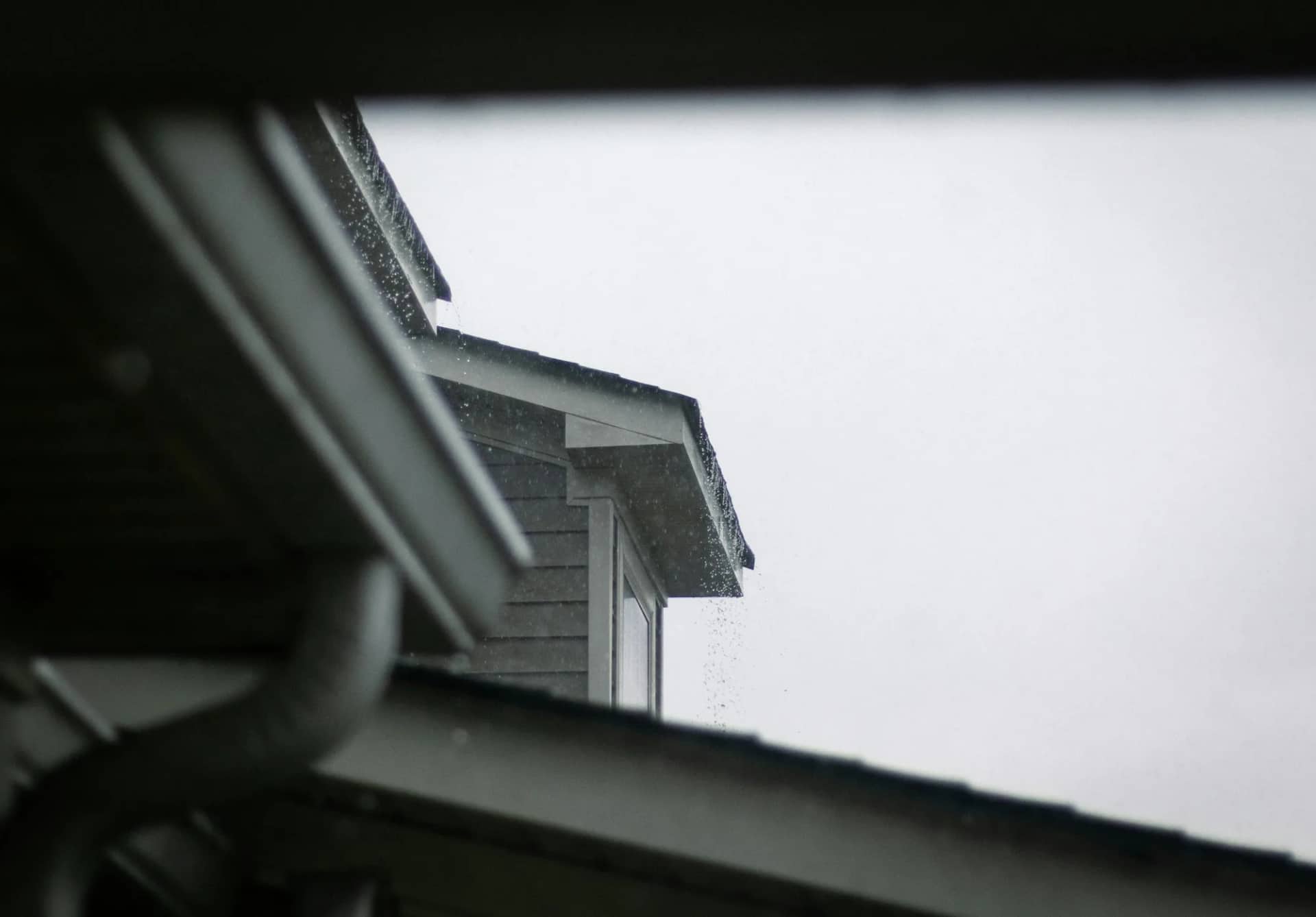 A roofline under a grey sky, the gutter running level along the fascia and the downpipe taking water away at the corner.
