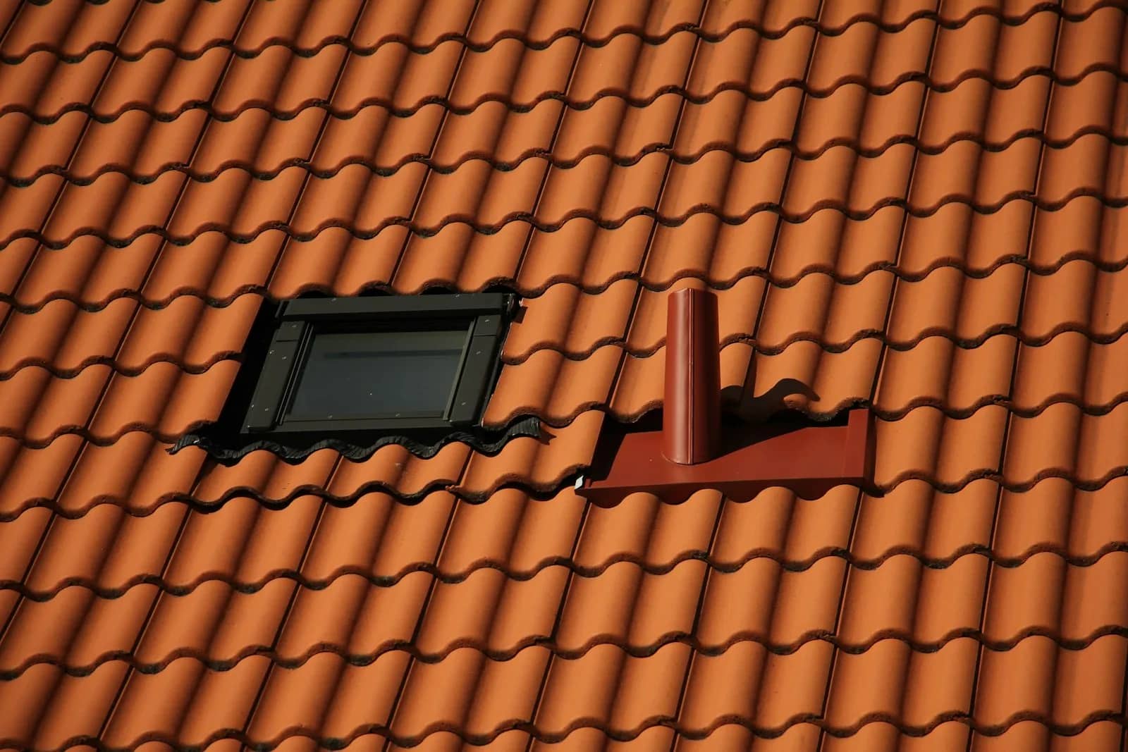 Roof cleaning: a skylight and a vent pipe set into a terracotta tiled slope, the tiles cut and closed around both upstands.