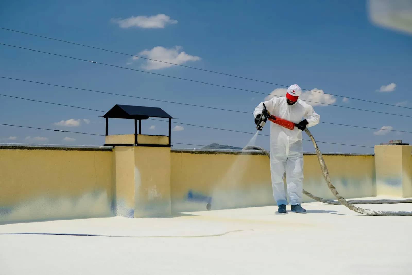 Roof cleaning: an operator in a white coverall laying an even spray across a roof surface from a hand lance, the treated area wet and pale behind the pass.