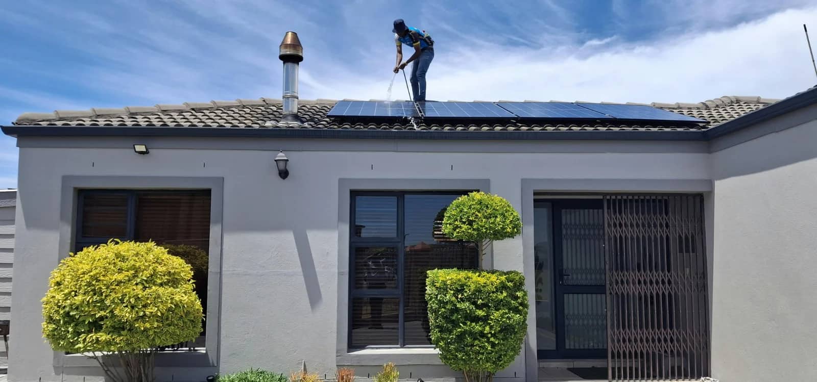 Roof cleaning: a worker on a pitched tile roof washing the surface down alongside a run of solar panels.