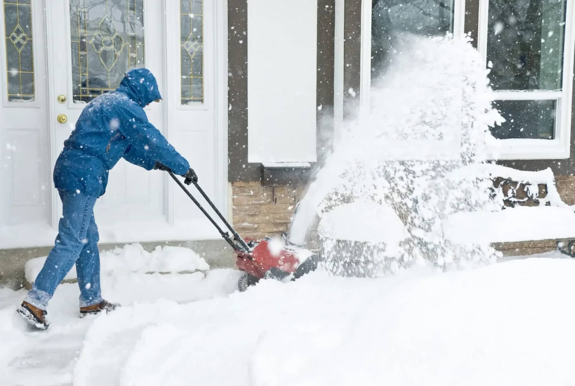Snow removal: an operator running a snowblower along a path, snow arcing away from the auger.