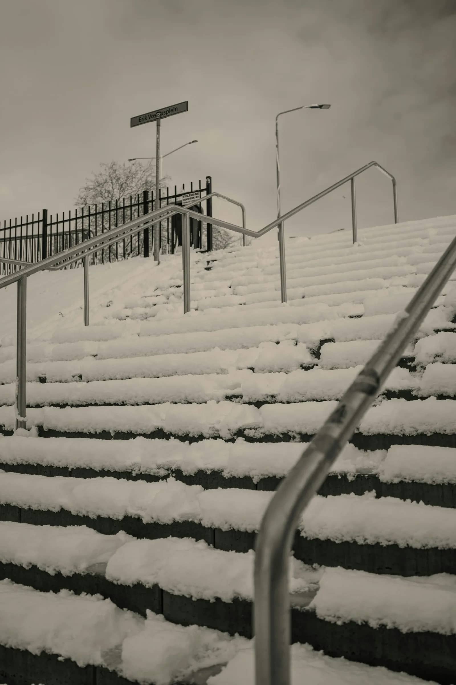 Snow removal: an outdoor flight of steps under unbroken snow, the metal handrail running down beside treads whose edges have disappeared.