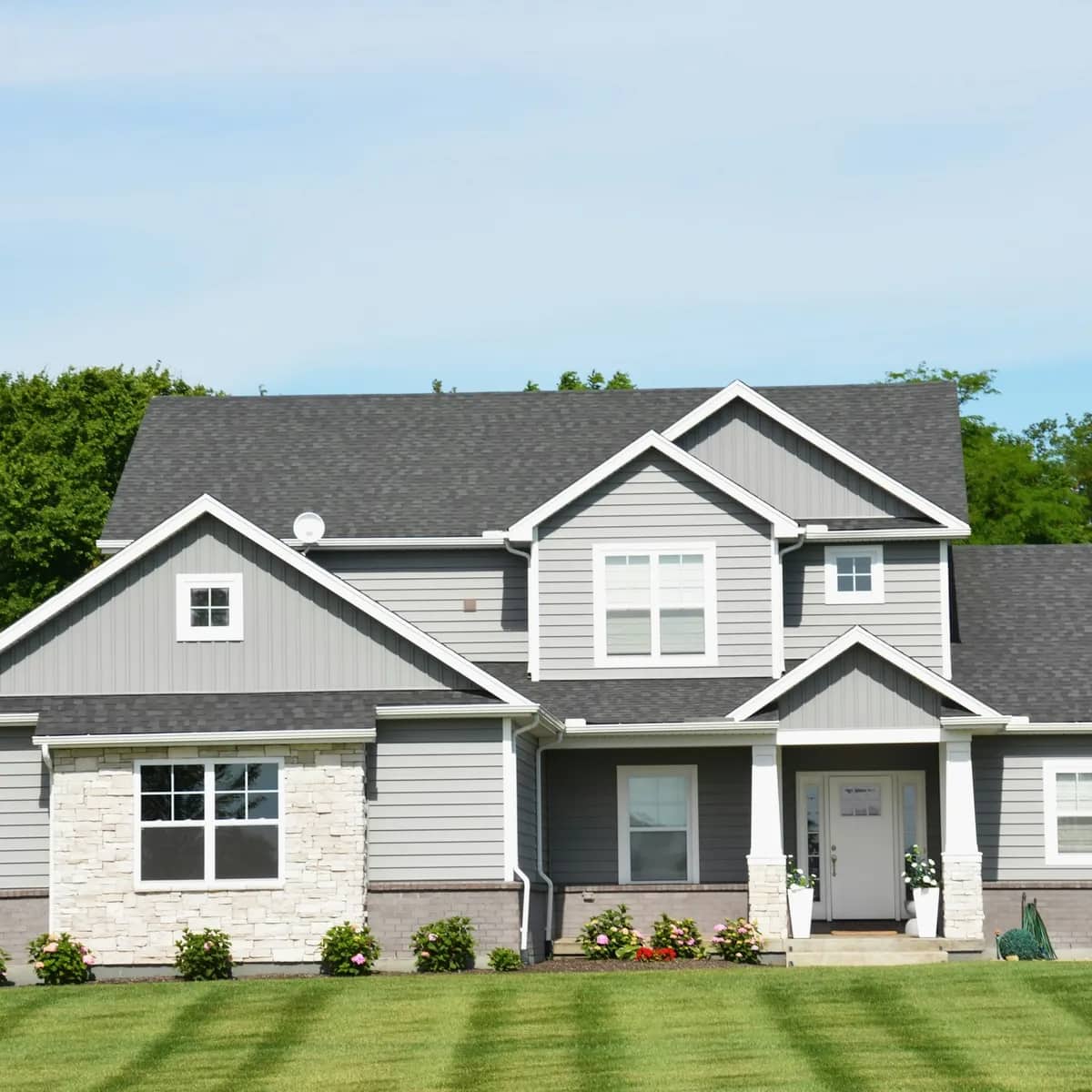 A grey two-storey house behind a freshly striped lawn and tidy flower beds.