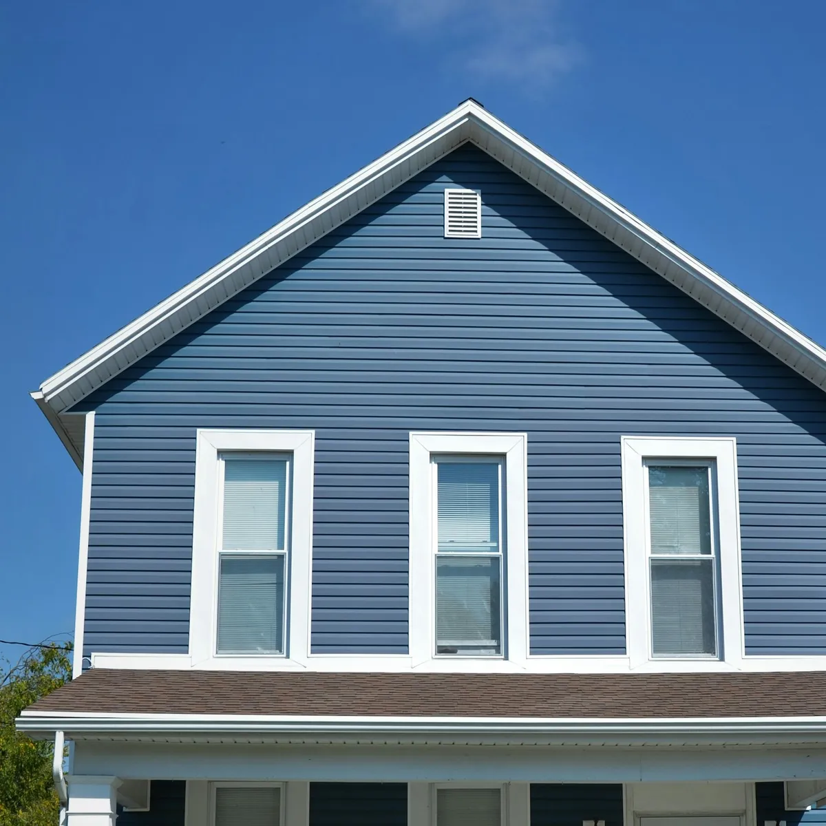 The upper storey of a house in blue lap siding with crisp white window trim and gable, under a clear sky.