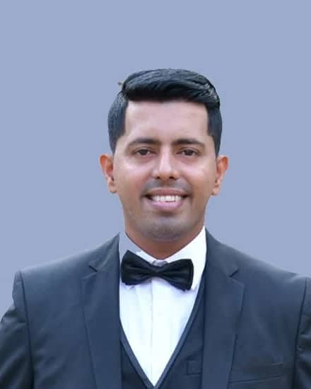 Wilson, co-founder of RainCity Property Maintenance, smiling in a dark suit and bow tie against a plain blue-grey backdrop.