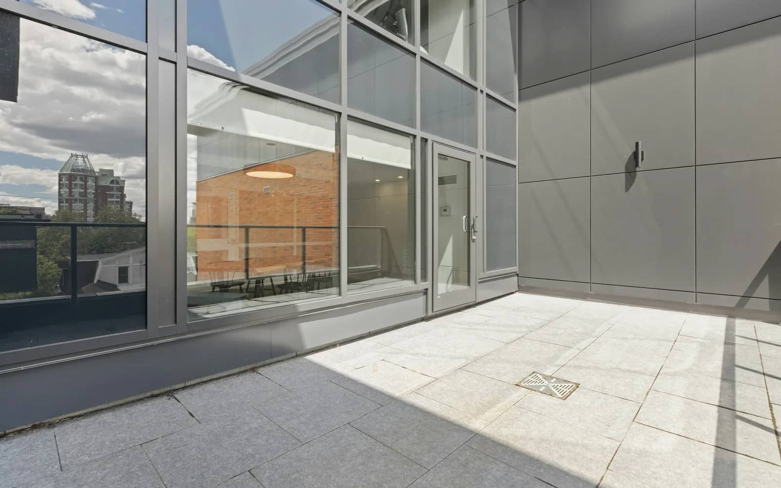Balcony cleaning: full-height glass doors and a grey panelled wall opening onto a paved rooftop terrace, a floor drain set into the pavers.