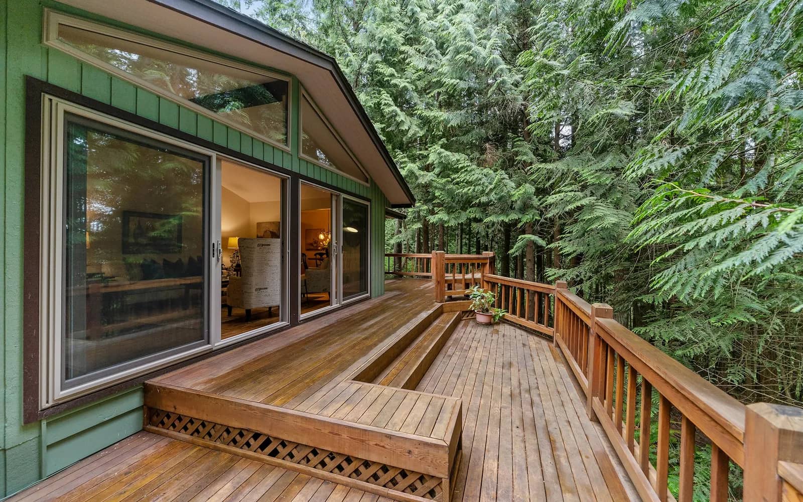 Balcony cleaning: a cedar deck and built-in bench off a green-sided house, sliding doors behind and tall conifers all around.