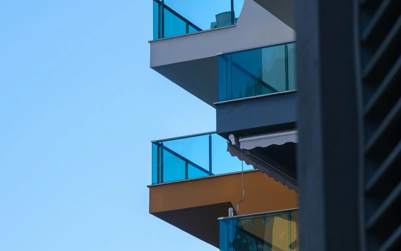 Balcony cleaning: glass-railed balconies stacked one above another up the corner of an apartment tower against a clear sky.