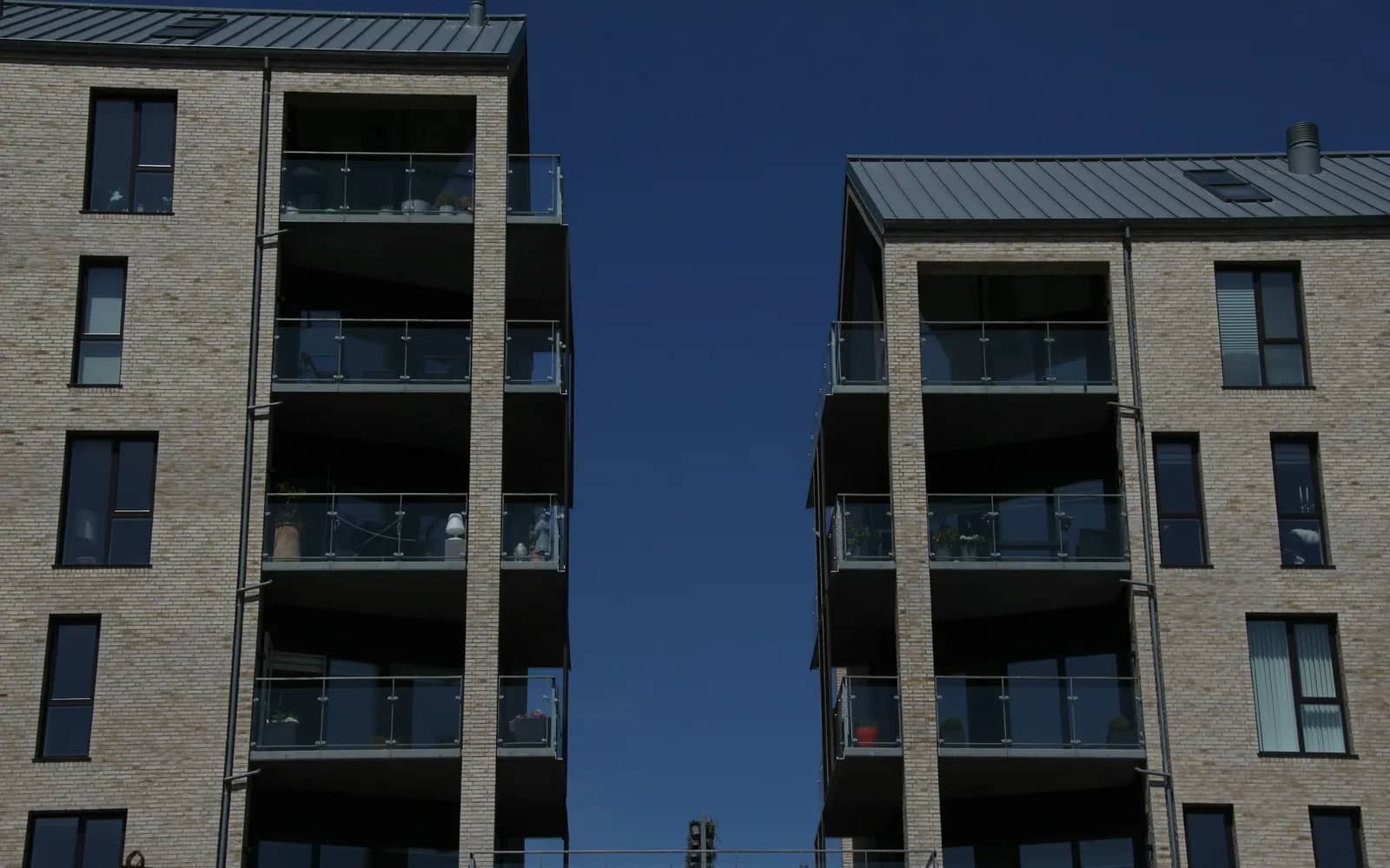 Balcony cleaning: two brick mid-rise apartment blocks with a column of glass-railed balconies on each, against a deep blue sky.