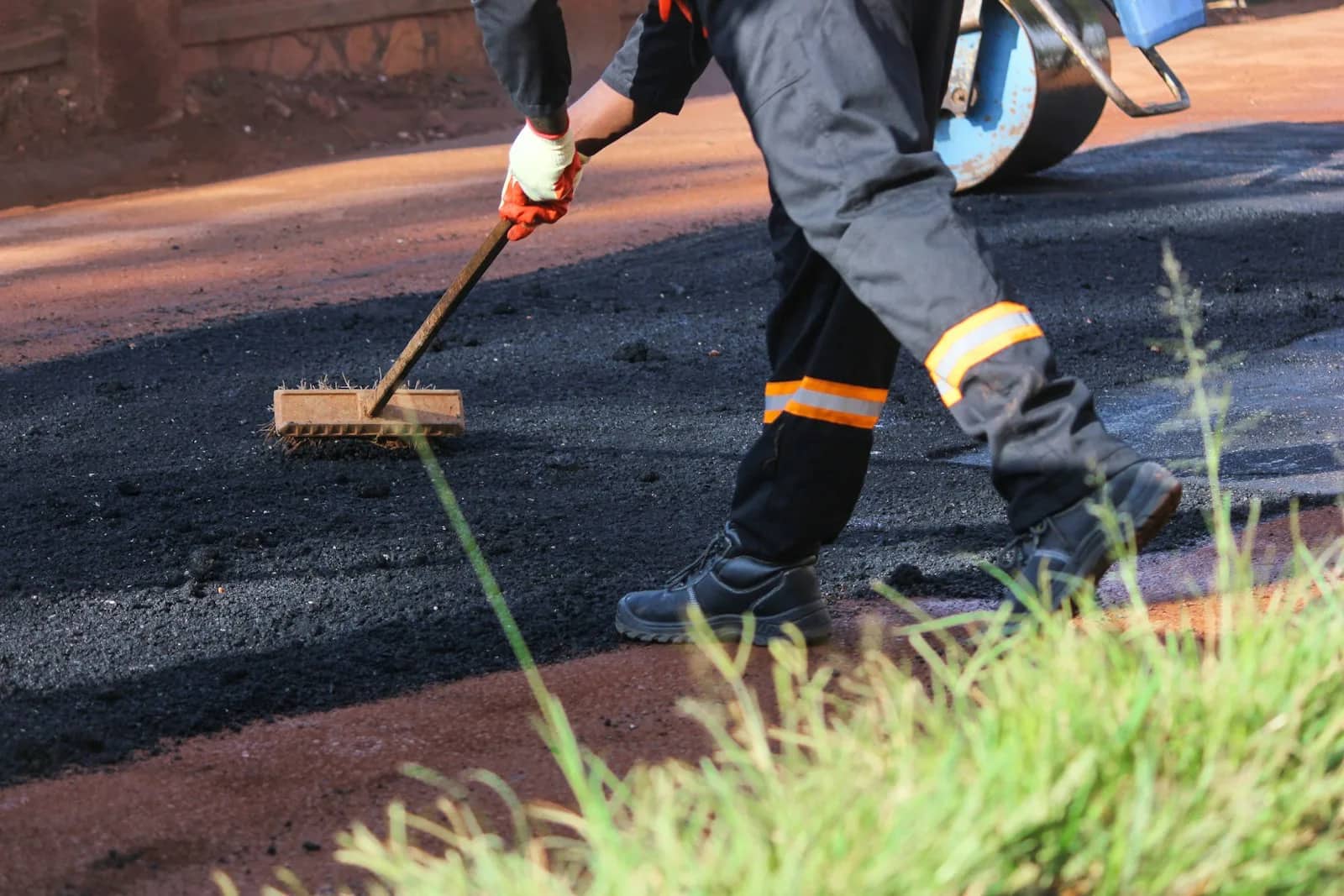 Concrete and asphalt sealing: an operator drawing a squeegee across asphalt, the sealed surface behind the head dark and wet against the paler surface still to be covered.