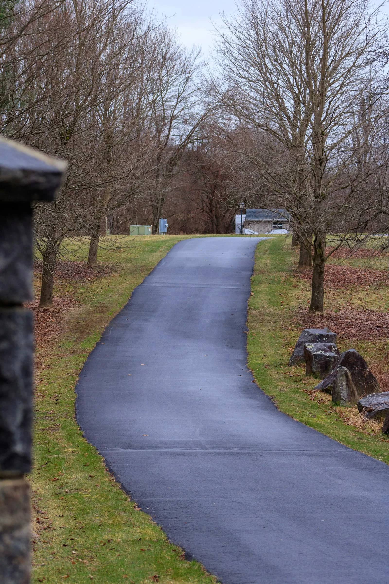 Concrete and asphalt sealing: a sealed walkway running through parkland, the surface unbroken and the edges holding a clean line against the grass either side.