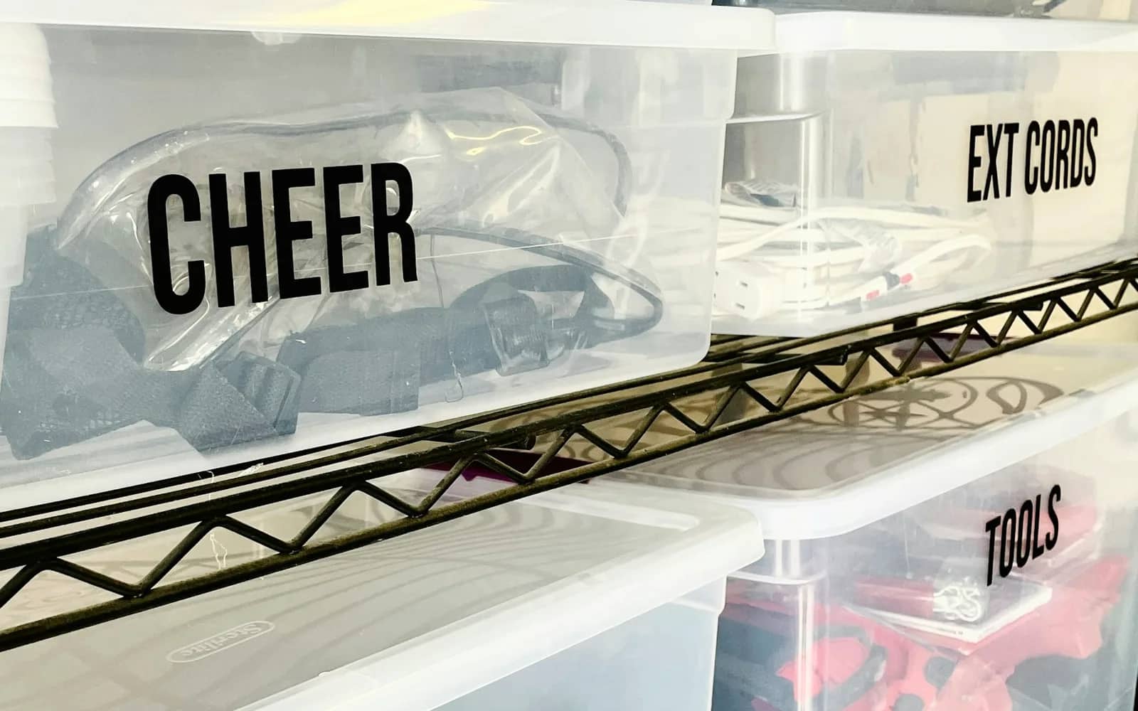 Holiday lights: clear lidded storage bins on a wire shelf, labelled CHEER, EXT CORDS and TOOLS.