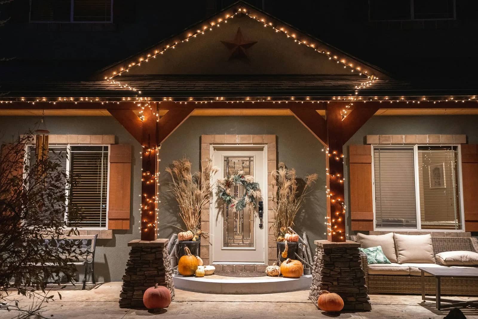 Holiday light installation: a covered porch lit along its eave and down the posts, with a wreath at the door and seating set out below.
