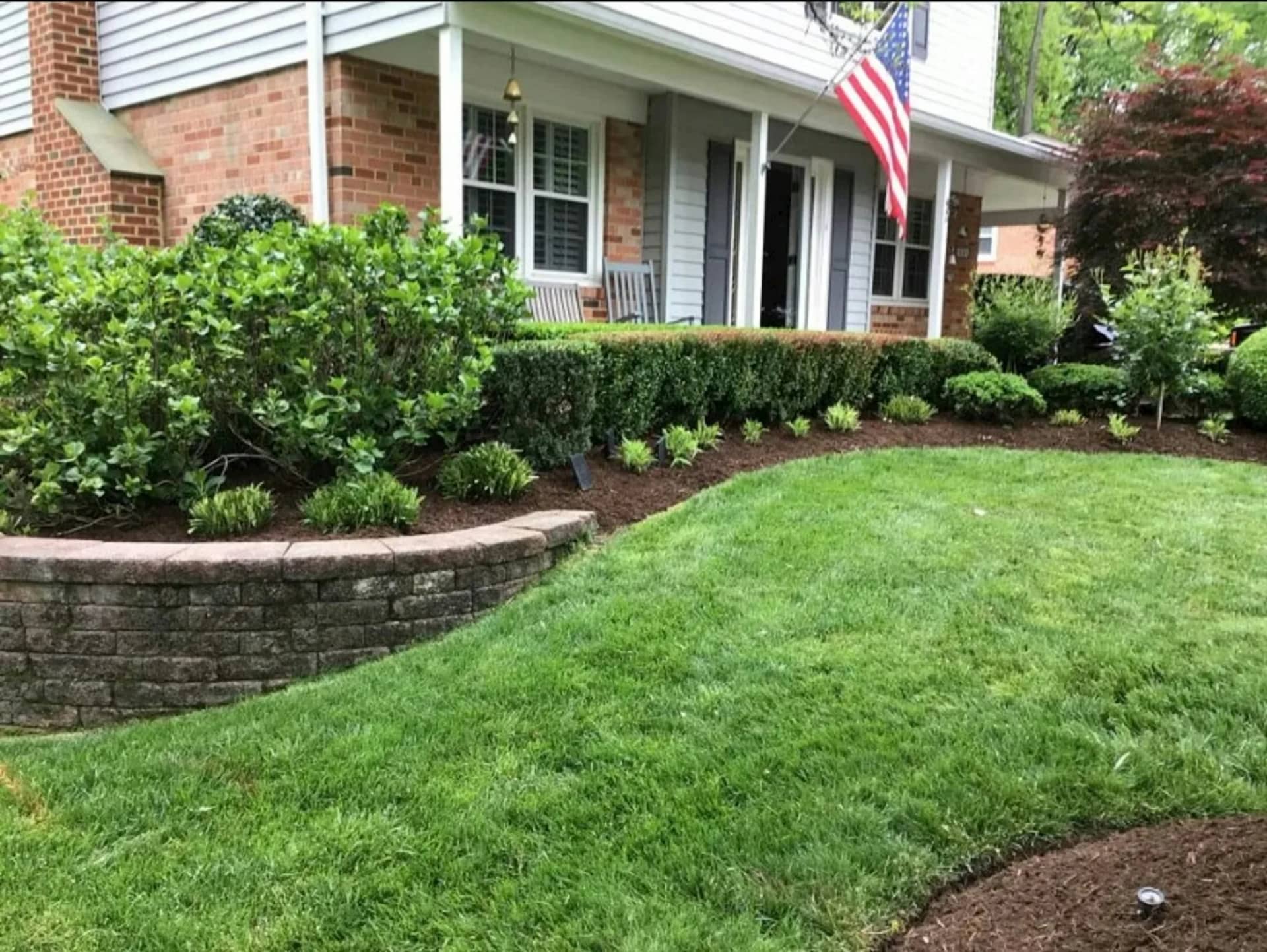 A house frontage with the lawn cut evenly to a low retaining wall, clipped shrubs set along the planting and every edge closed off.