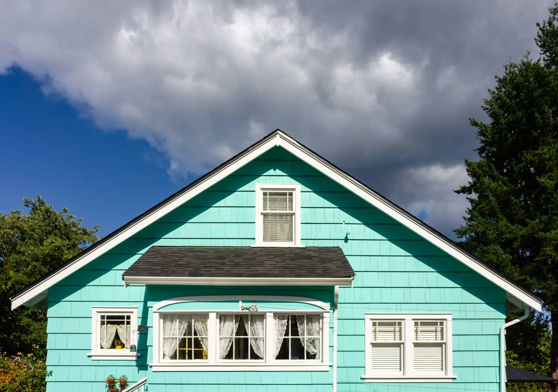A painted timber house under a bright sky, the body colour running clean to the white window trim and gable boards with every line held straight.