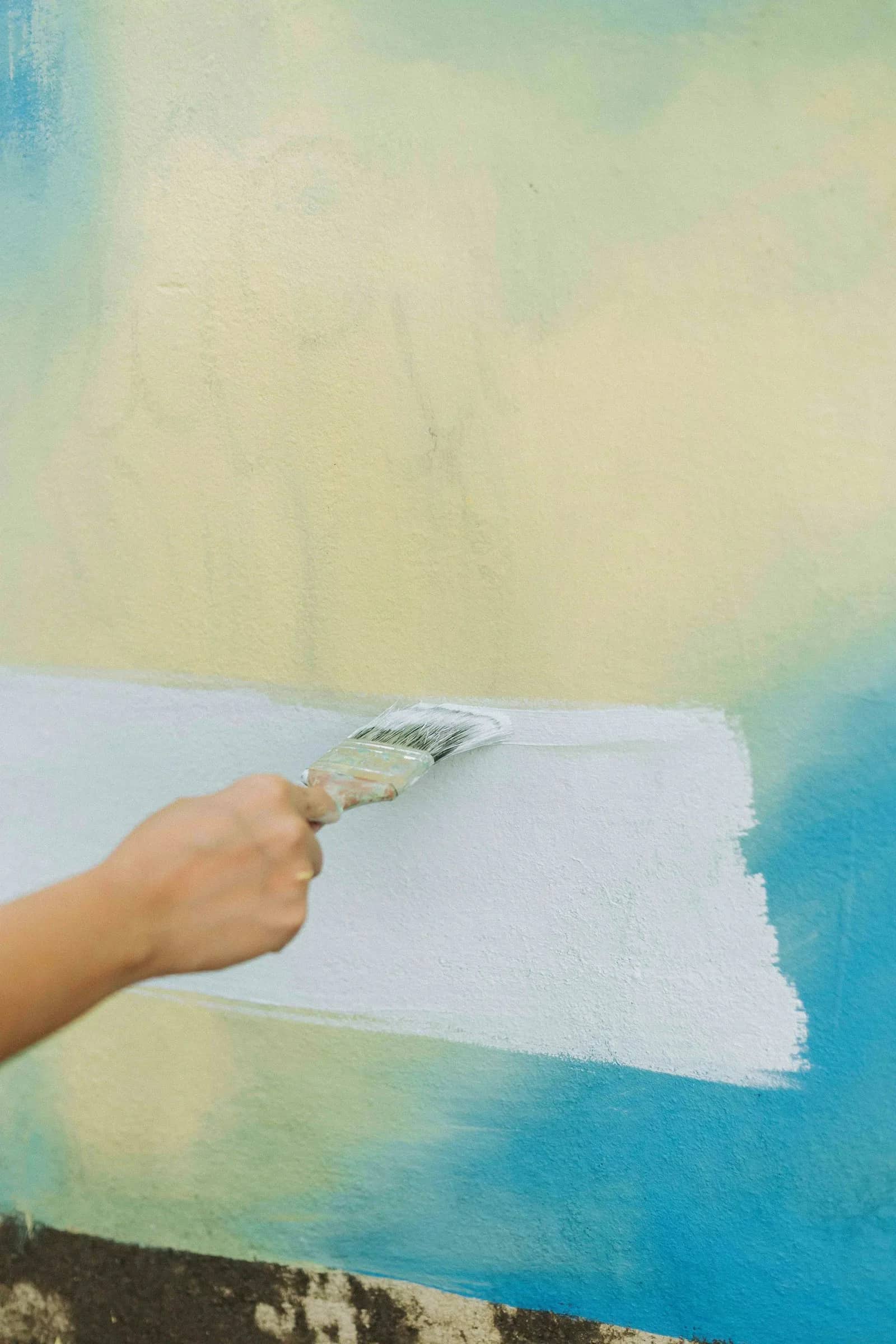 Painting: a brush drawn along the boundary between a pale new coat and the colour underneath, the wet edge left clean and straight across the wall.