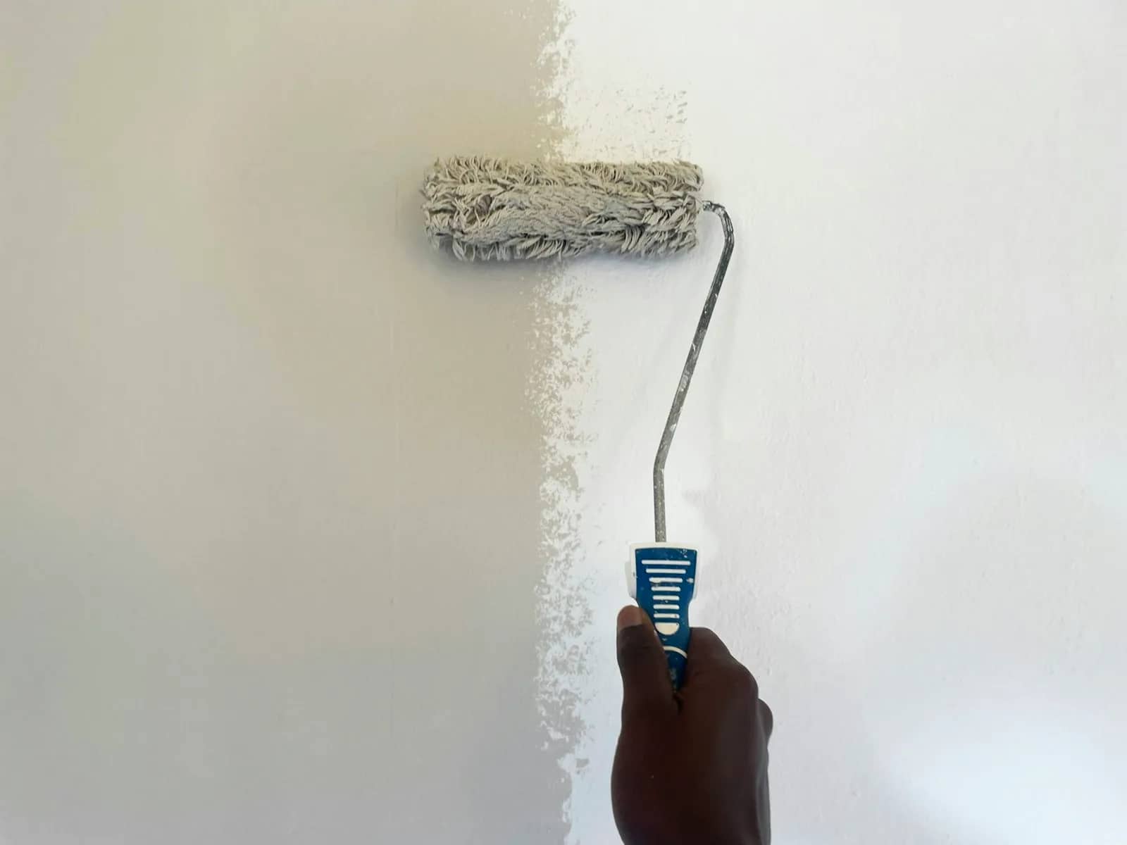 Painting: a roller laying a pale coat across a wall, the covered band standing out against the older finish still showing to one side.
